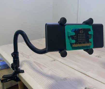 A black gooseneck mount is clamped the edge of a table. A micro:bit is attached via a 3d-printed mounting clamp at the end of the flexible arm, to allow for easy access and operation.