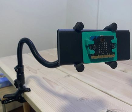 A black gooseneck mount is clamped the edge of a table. A micro:bit is attached via a 3d-printed mounting clamp at the end of the flexible arm, to allow for easy access and operation.