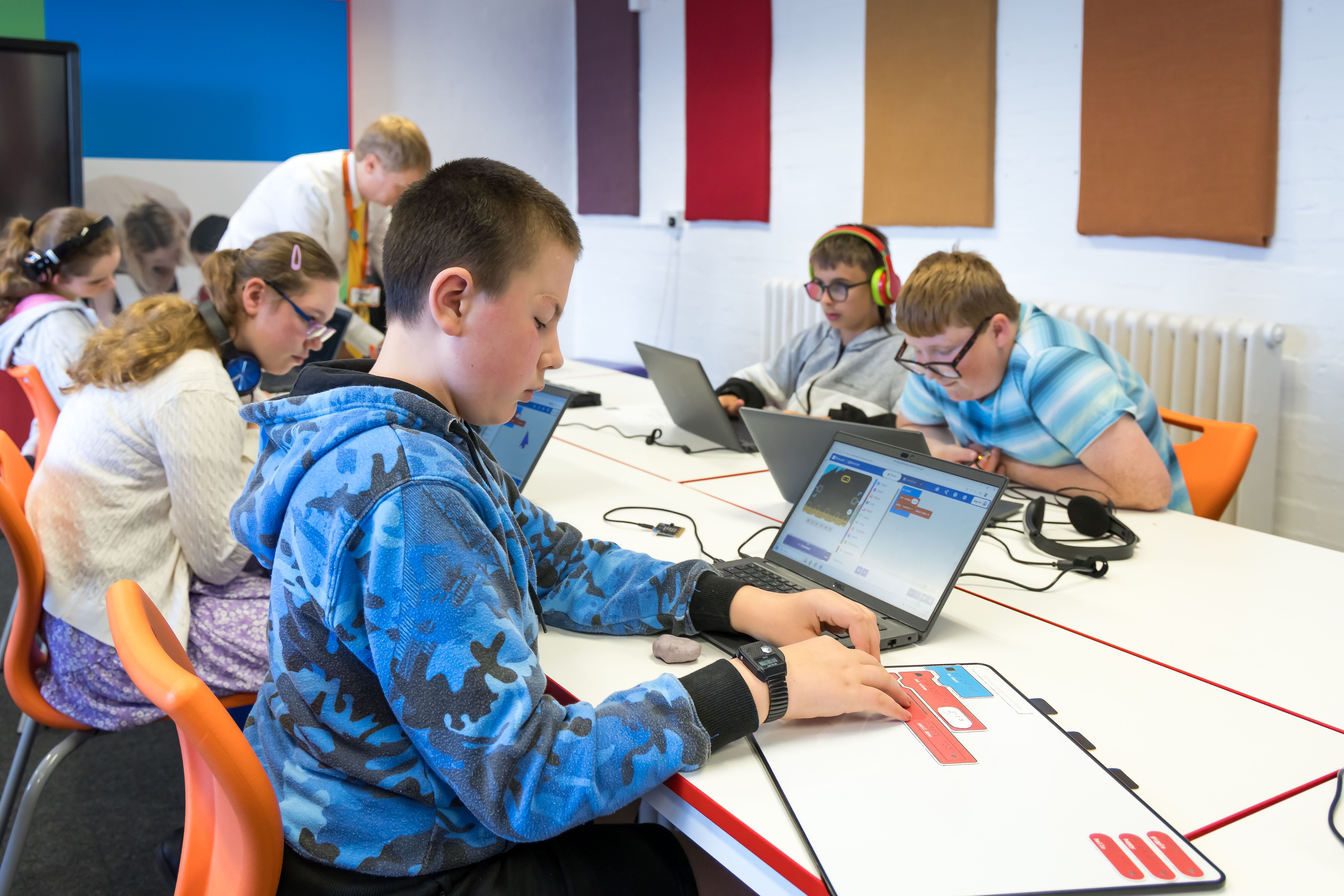 A student feeling tactile code blocks while the corresponding MakeCode Start sound project is open on a laptop in front of the student.