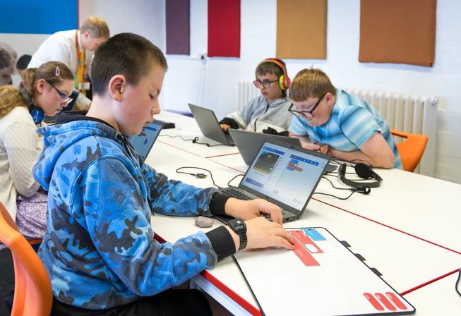 A student feeling tactile code blocks while the corresponding MakeCode Start sound project is open on a laptop in front of the student.