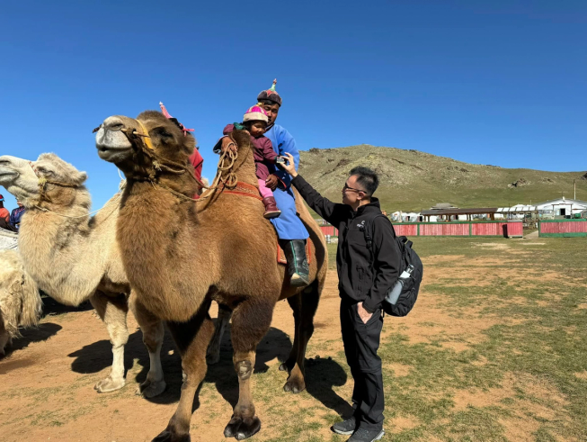 Father and daughter sat on a camel in Mongolia as Waris Candra (head of APAC) shows them a micro:bit)