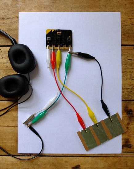 صورة تظهر كيفية توصيل فواصل الرغاوي الفضية مع دبابيس micro:bit 1 و 2 و GND