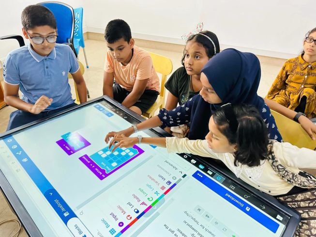 Children gather around a giant touchscreen to get coding with the micro:bit