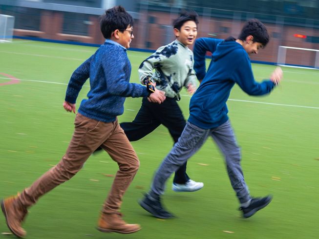 Three students run across the field, micro:bits attached to their wrists