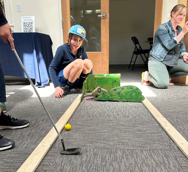 Someone hits a golf ball towards a structure of the lizard with an open mouth