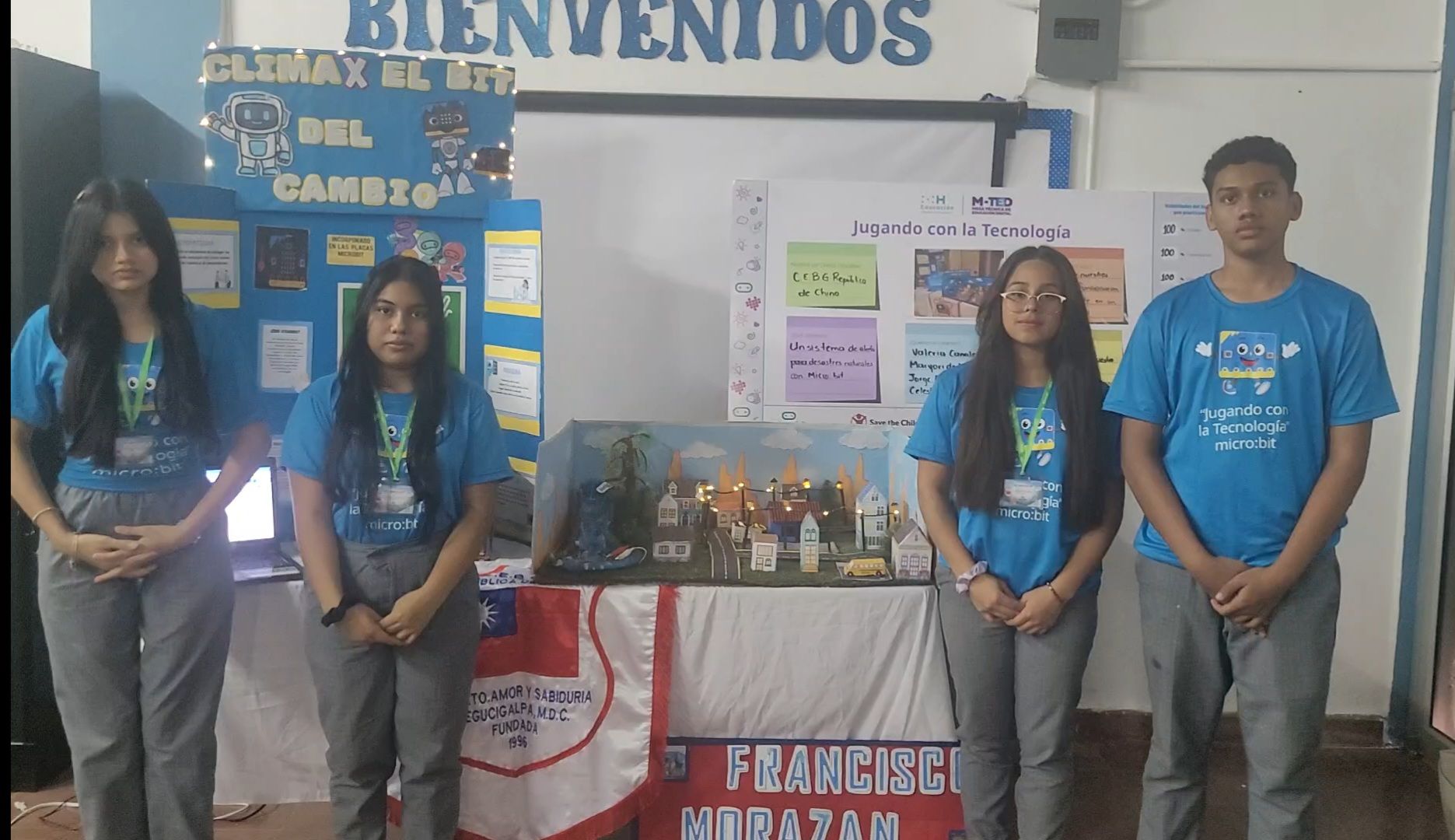 Students stand in front of a table with the alert system prototype and posters about their project.
