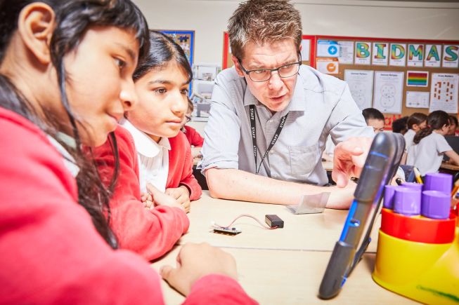 Teacher demonstrating how to use a micro:bit with a tablet to 2 pupils