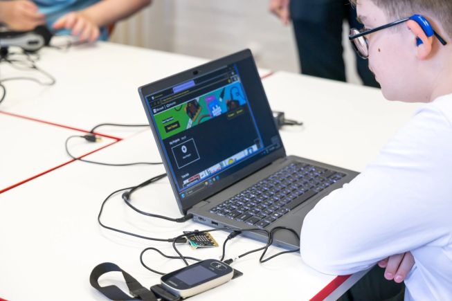 A student who is deaf or hard of hearing uses assistive hearing technology while coding with the micro:bit in Microsoft MakeCode.