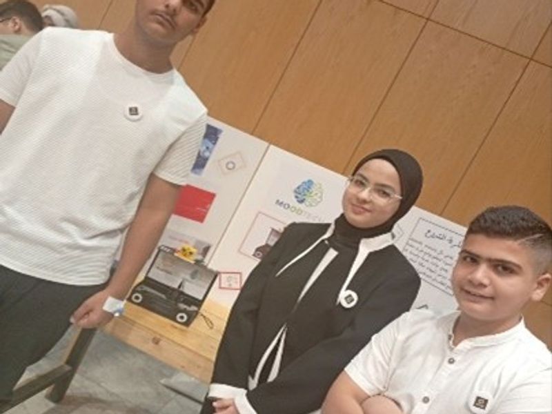 Students stand next to a poster and prototype of their project.