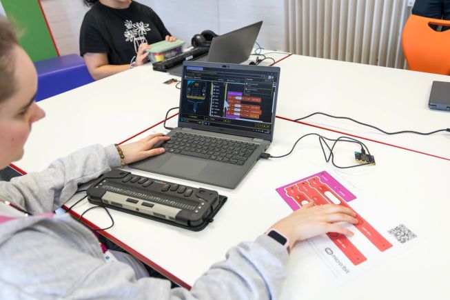 A student explores a program using a tactile diagram of the program whilst using screen reader and refreshable braille display to also explore the same program in MakeCode.