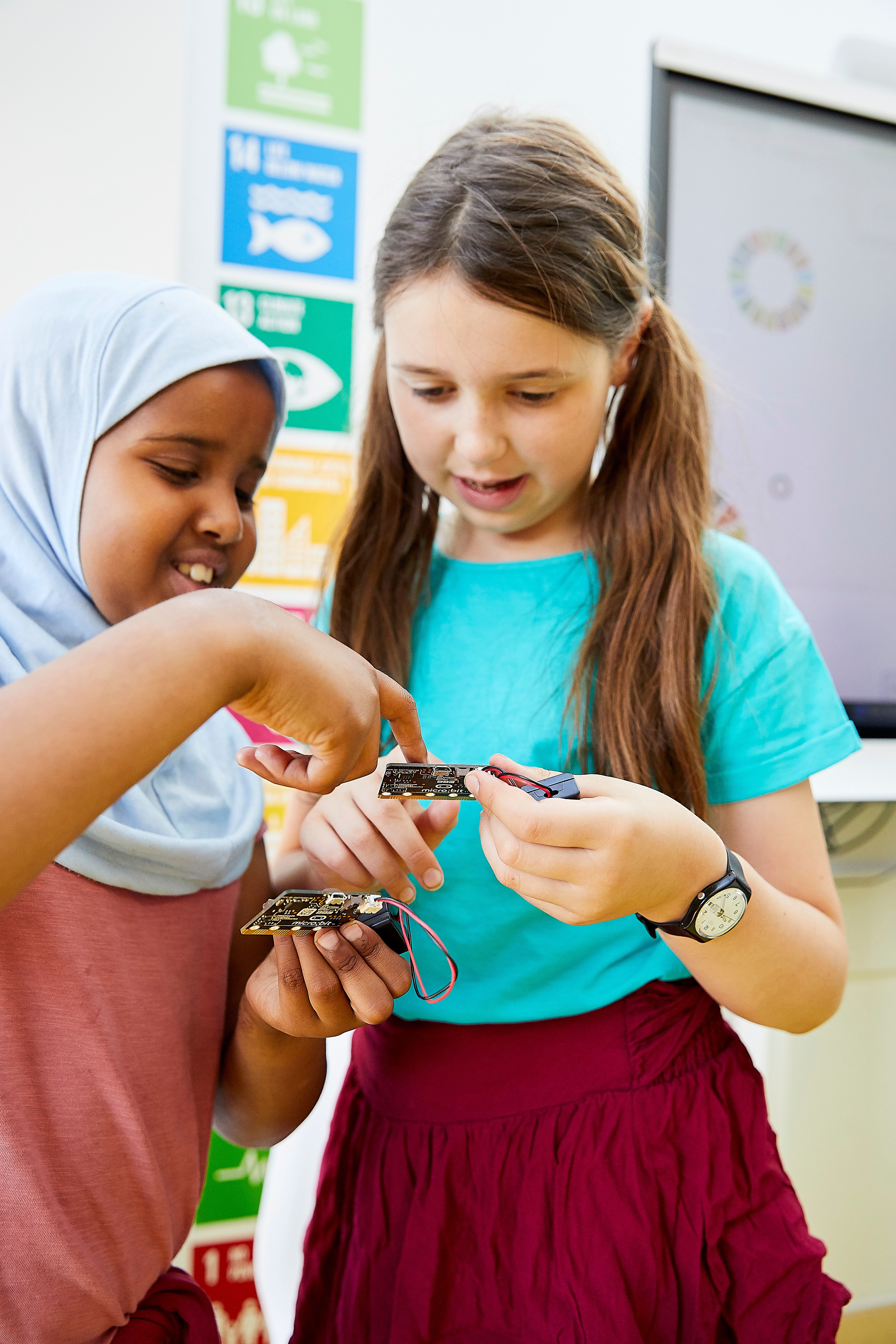 Two girls holding a micro:bit and discussing them, pressing buttons and smiling