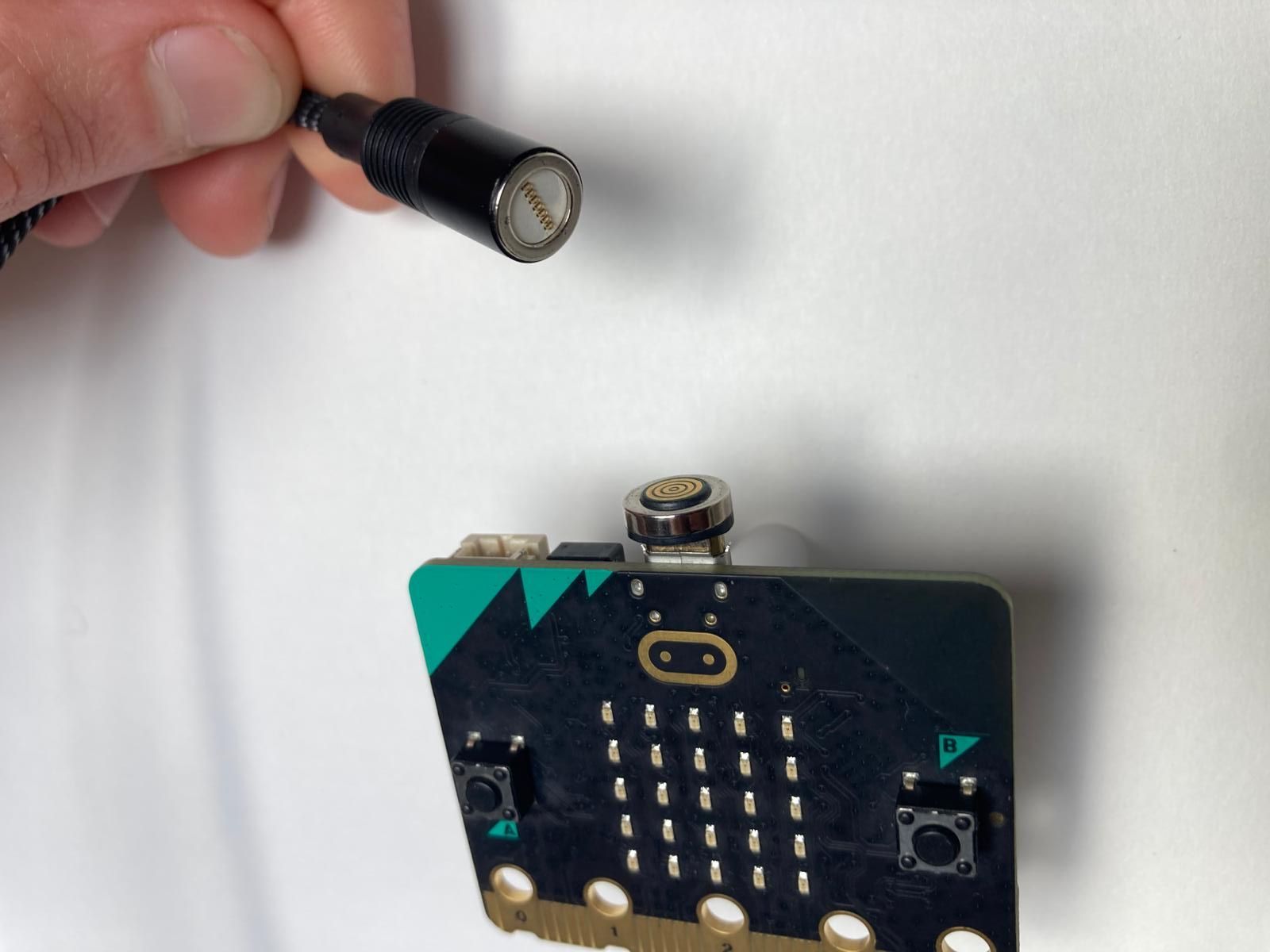 A photo of a magnetic USB cable adaptor. The end part is already attached to the micro USB port on the micro:bit and the cable will snap on magnetically.