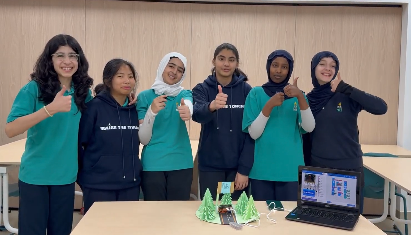 Students smile and show a thumbs up standing behind the solar powered car prototype.