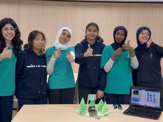 Students smile and show a thumbs up standing behind the solar powered car prototype.