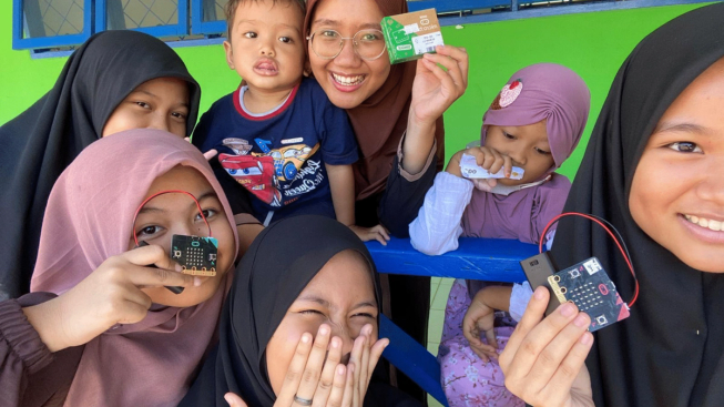 Several enthusiastic teenage girls holding micro:bits with two younger pupils in a classroom in Indonesia
