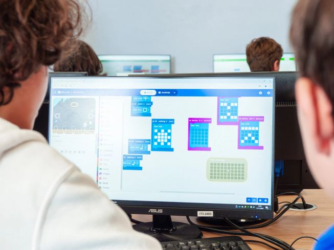 Two students look at a screen, editing code with Microsoft MakeCode