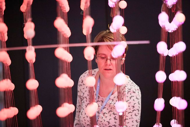 Woman stands next to cube of pink lights
