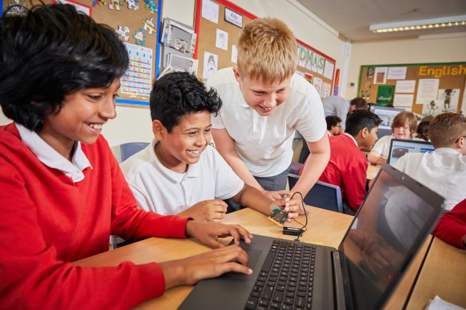 Three boys laugh as they enjoy coding with micro:bits in their classroom