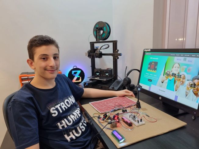 Zayd sitting at his desk with he prototype in front of him and his design on his screen