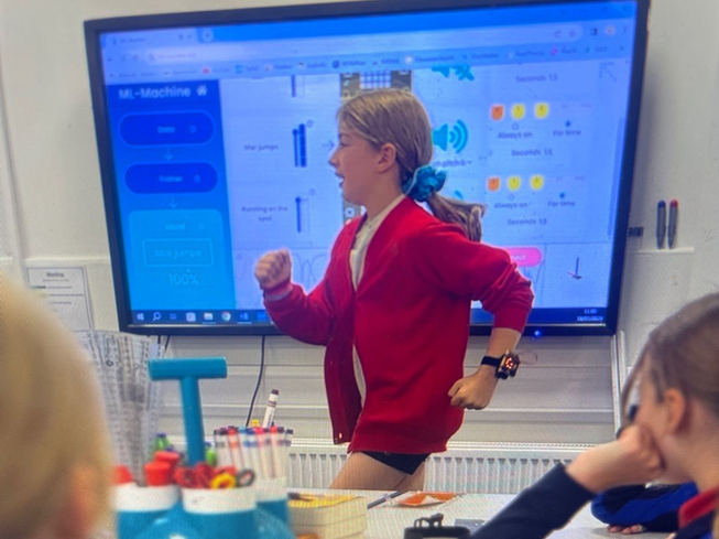 Primary school pupil, a girl, moving as if walking on the spot while wearing a micro:bit on her wrist.