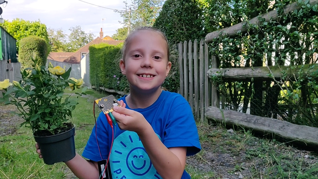Child showing micro:bit plant moisture project in their garden