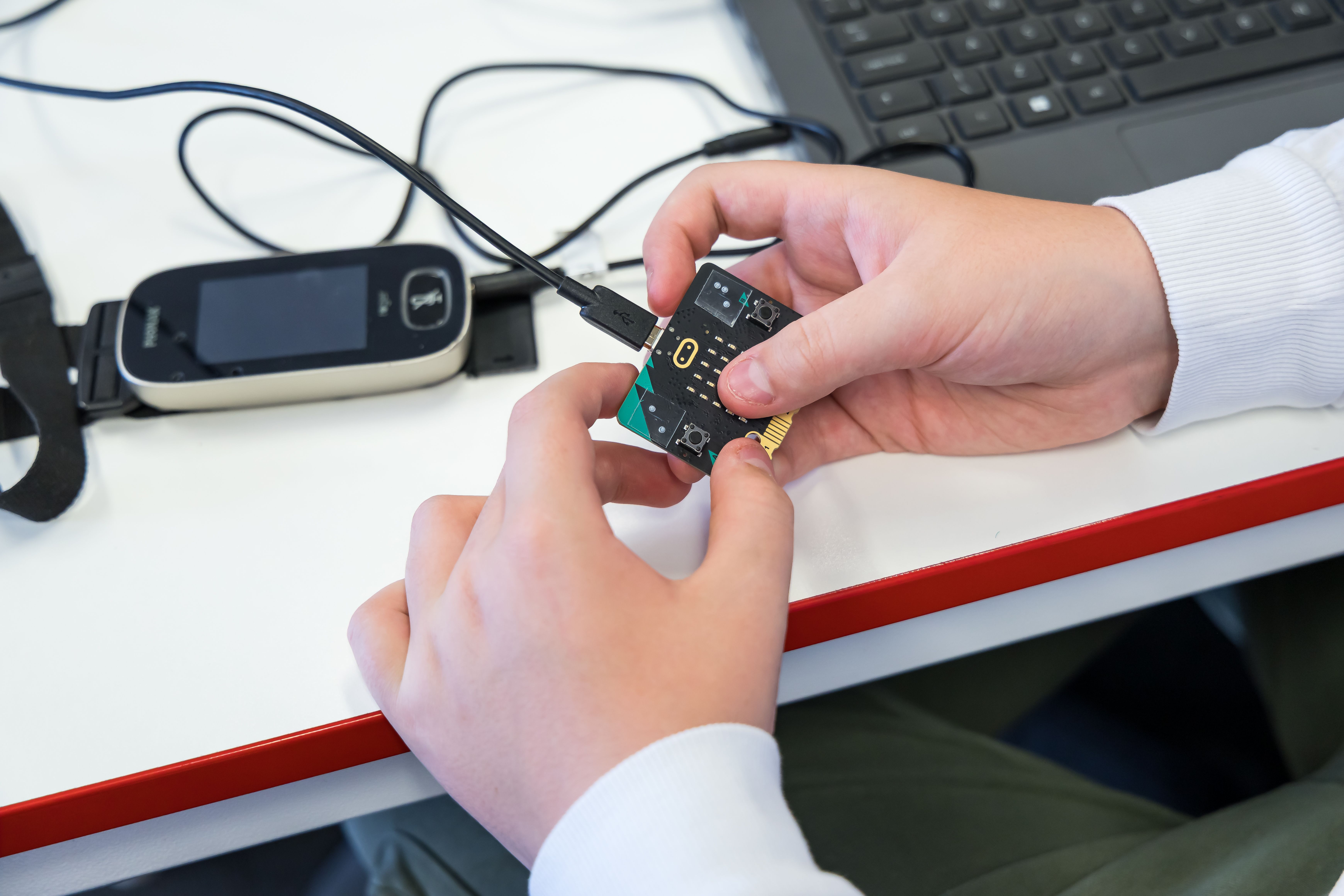 A pair of hands holding a micro:bit with a USB cable attached at the top