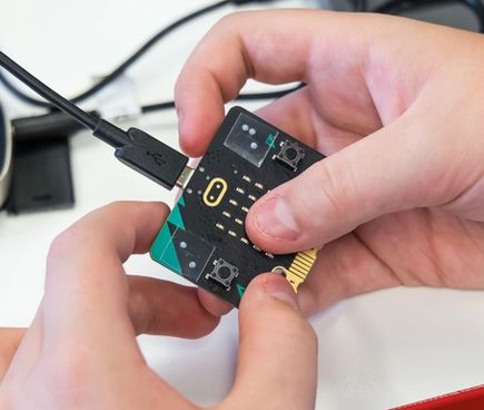 A pair of hands holding a micro:bit with a USB cable attached at the top