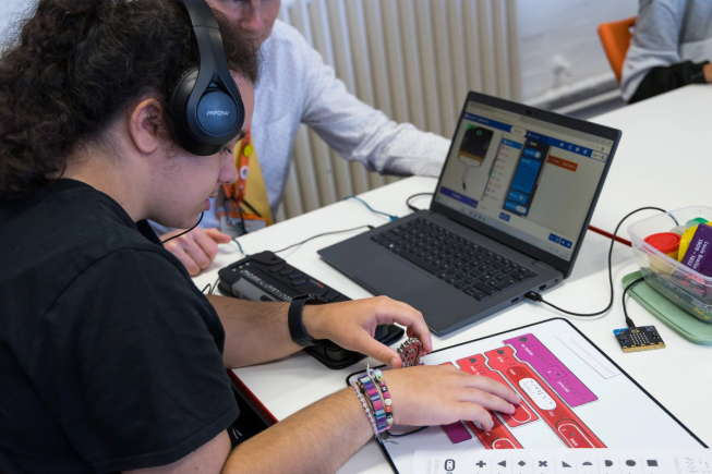 A student explores a tactile completed program whilst working on the same program in MakeCode supported by a teacher.