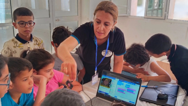 Samira Affi oversees a group of young students, who crowd around a laptop and a micro:bit, excitedly coding a beating heart project