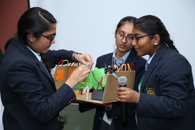 Image of three female students working on a prototype project made using cardboard, a micro:bit, alligator/crocodile clips and other materials. 