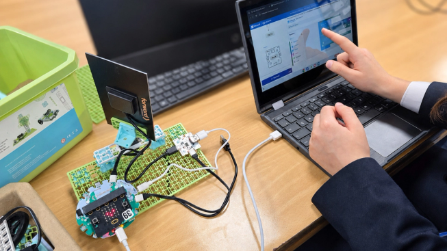 A pupil uses a touchscreen laptop connected to a micro:bit and electronic components during a physical computing activity.
