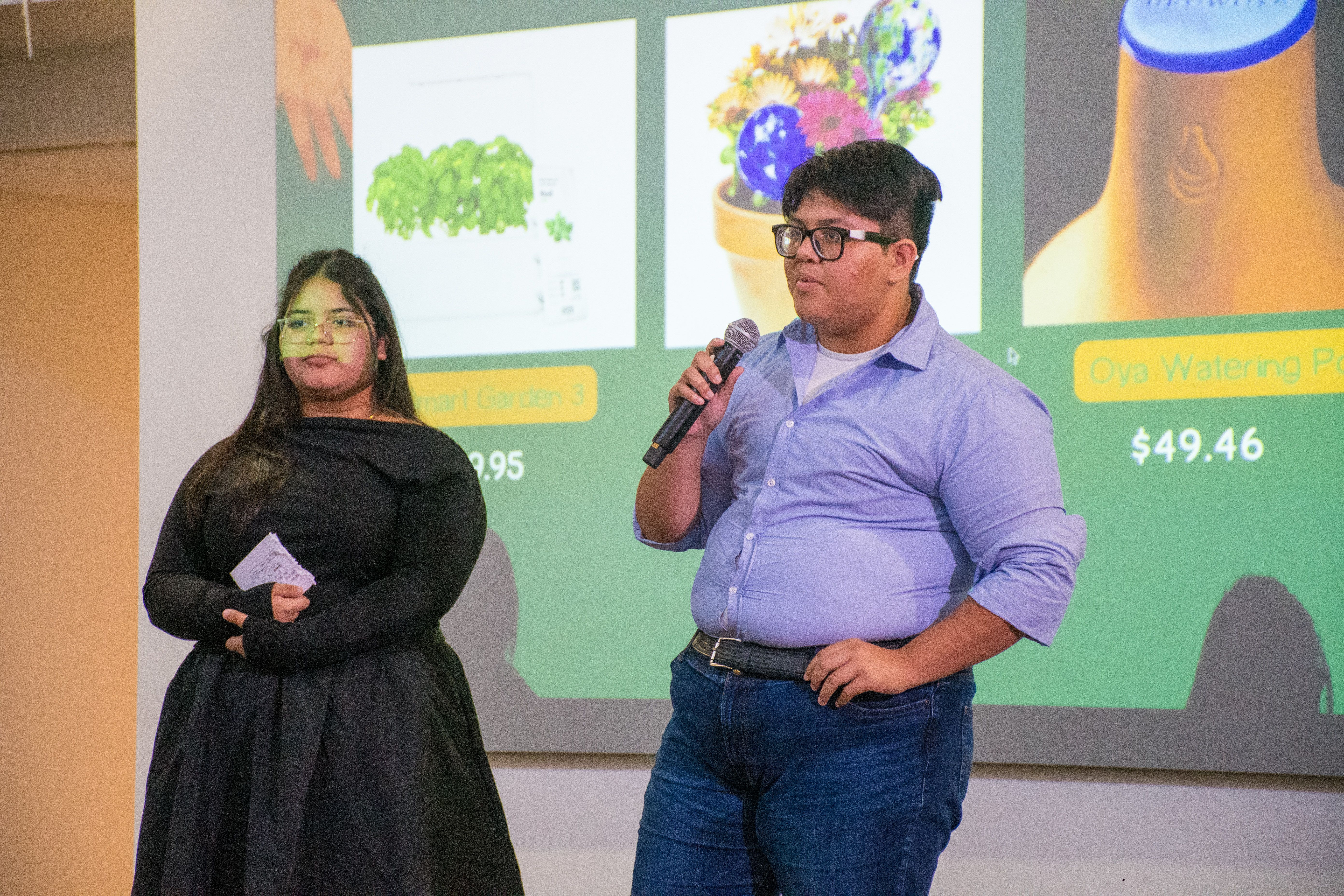 Students present their Microgarden project in front of a screen with a microphone.