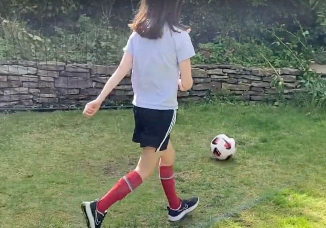 A girl about to kick a football on grass