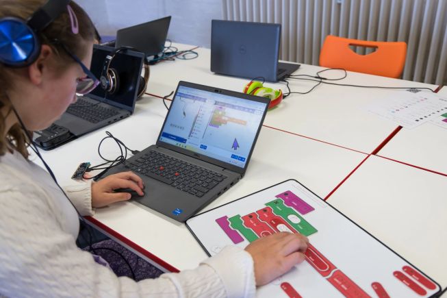 A student feeling tactile code blocks while the corresponding MakeCode Shake alarm project is open on a laptop in front of them.