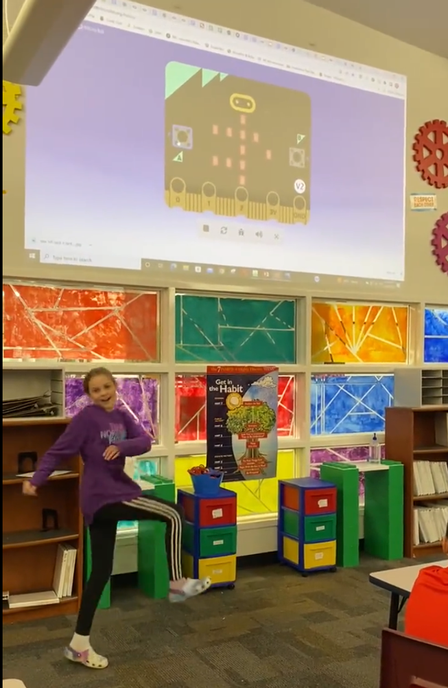 A girl dances in front of a screen, showing a micro:bit simulator displaying stickperson dance moves. The girl is repeating the moves superbly! Maryville Middle School, Missouri USA, from @bwynne22