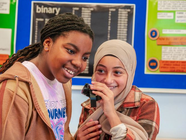 Two girls examine their micro:bit closely