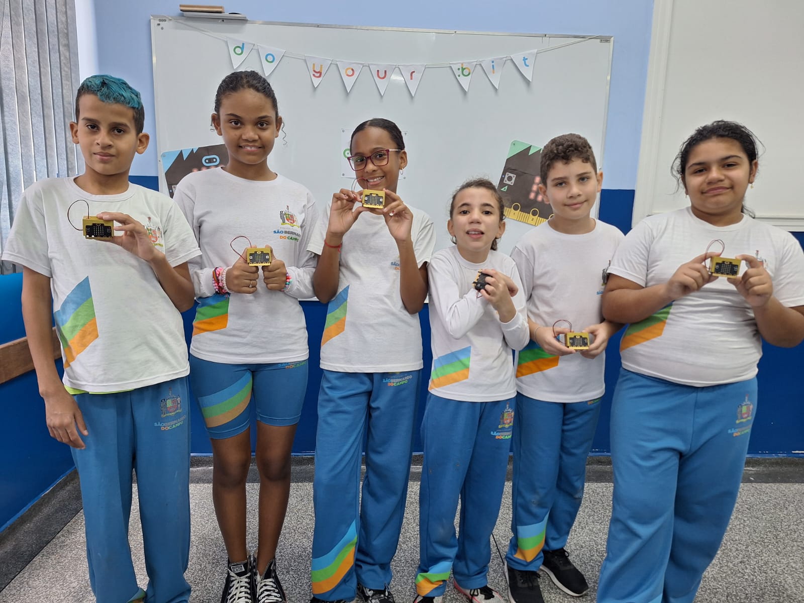 Students pose holding micro:bits in their classroom.