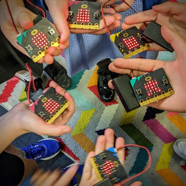 Six students from Malvern Wells Primary School, UK, stand in a circle holding their micro:bits, which are all loaded with music.