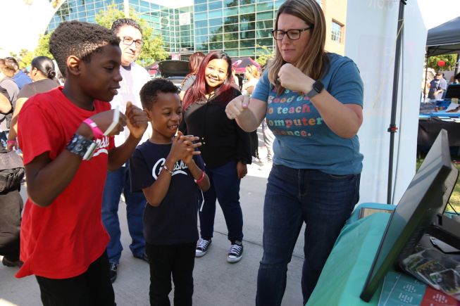 At STEAMfest, a micro:bit teacher shows two children how to move, as they have micro:bits strapped to their wrists to track movement