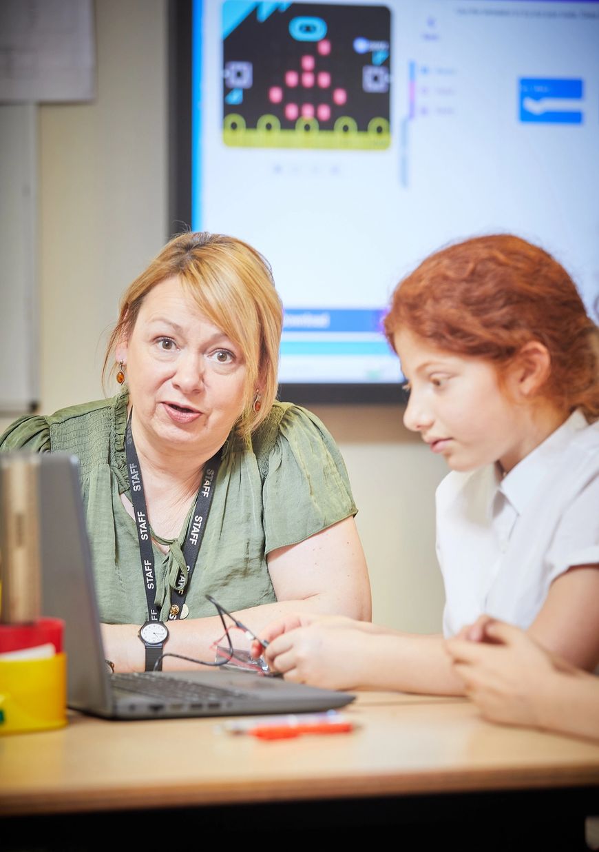 Nuczycielka siedząca z uczniem wyjaśniająca, jak działa micro:bit