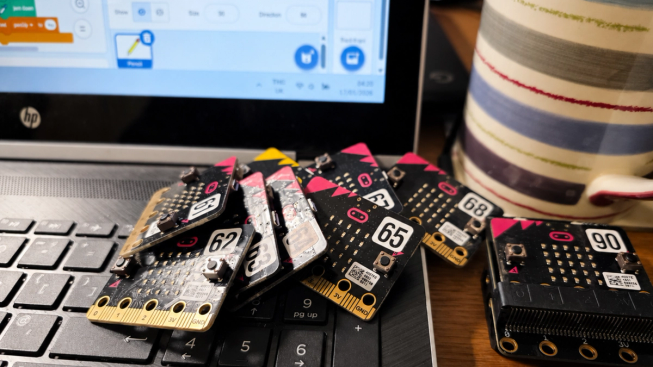 A collection of numbered micro:bits sits on a laptop keyboard in front of a coding screen.