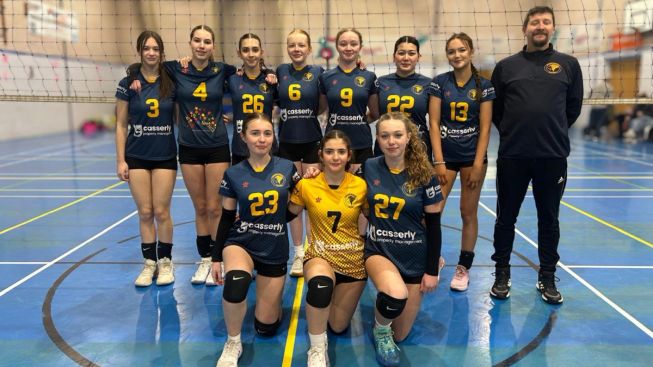 Girls’ volleyball team posing together on an indoor court in navy and yellow uniforms, with their coach standing to the side.