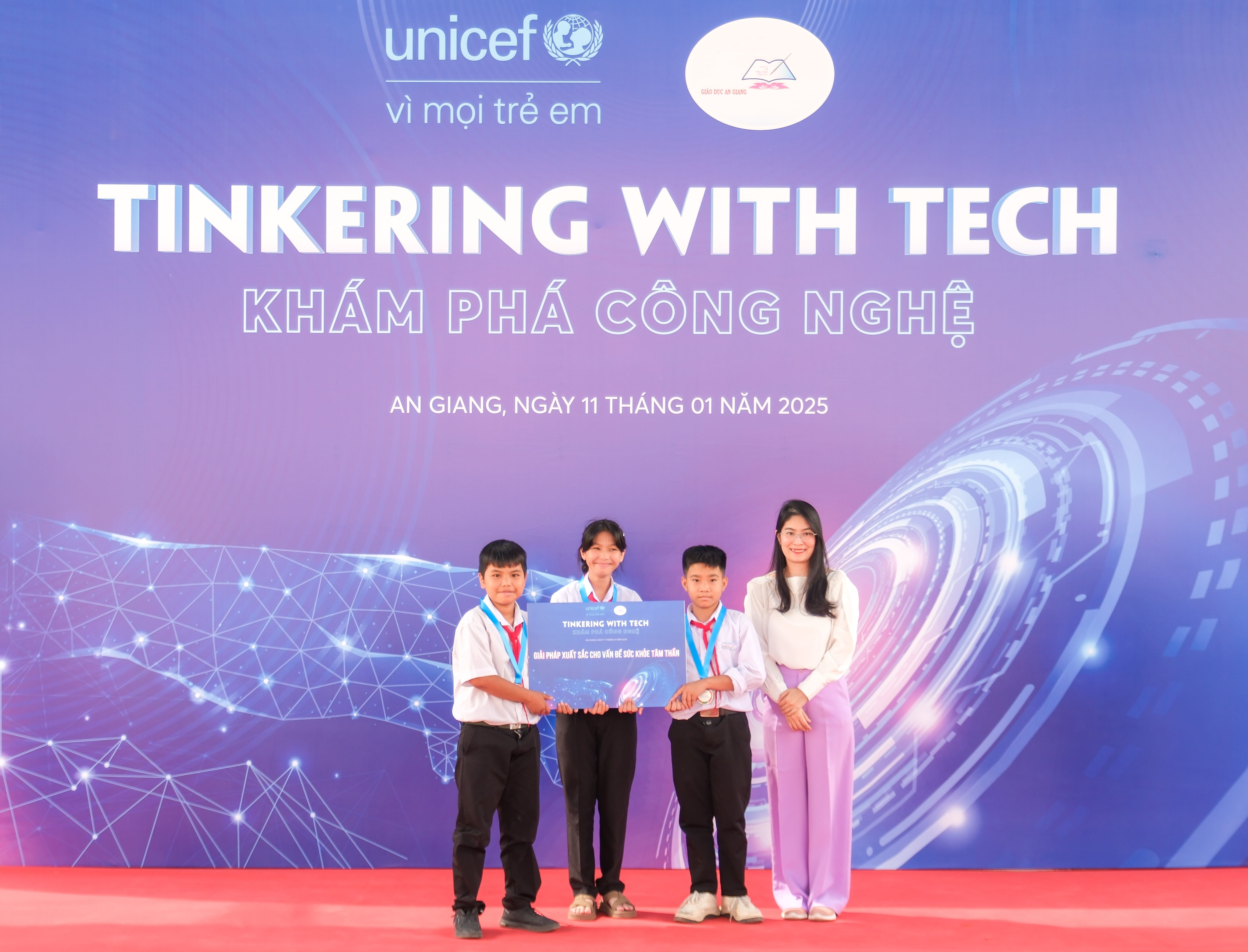 Students pose in front of a sign that says &quot;Tinkering with Tech&quot;