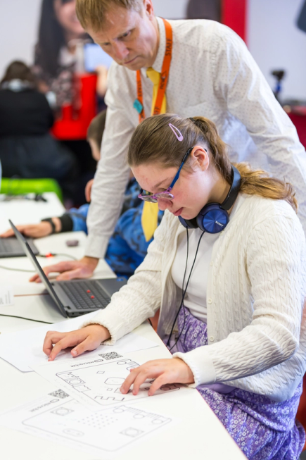 Supported by a teacher, a girl explores a tactile diagram of the back of the micro:bit using a braille embossed key.