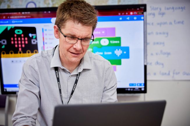 A teacher is looking at a laptop screen, intently planning their next academic year with micro:bit