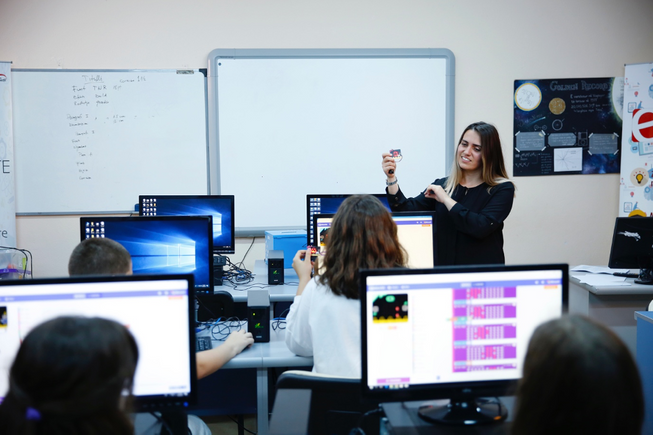 A teacher in front of a class holding up a micro:bit