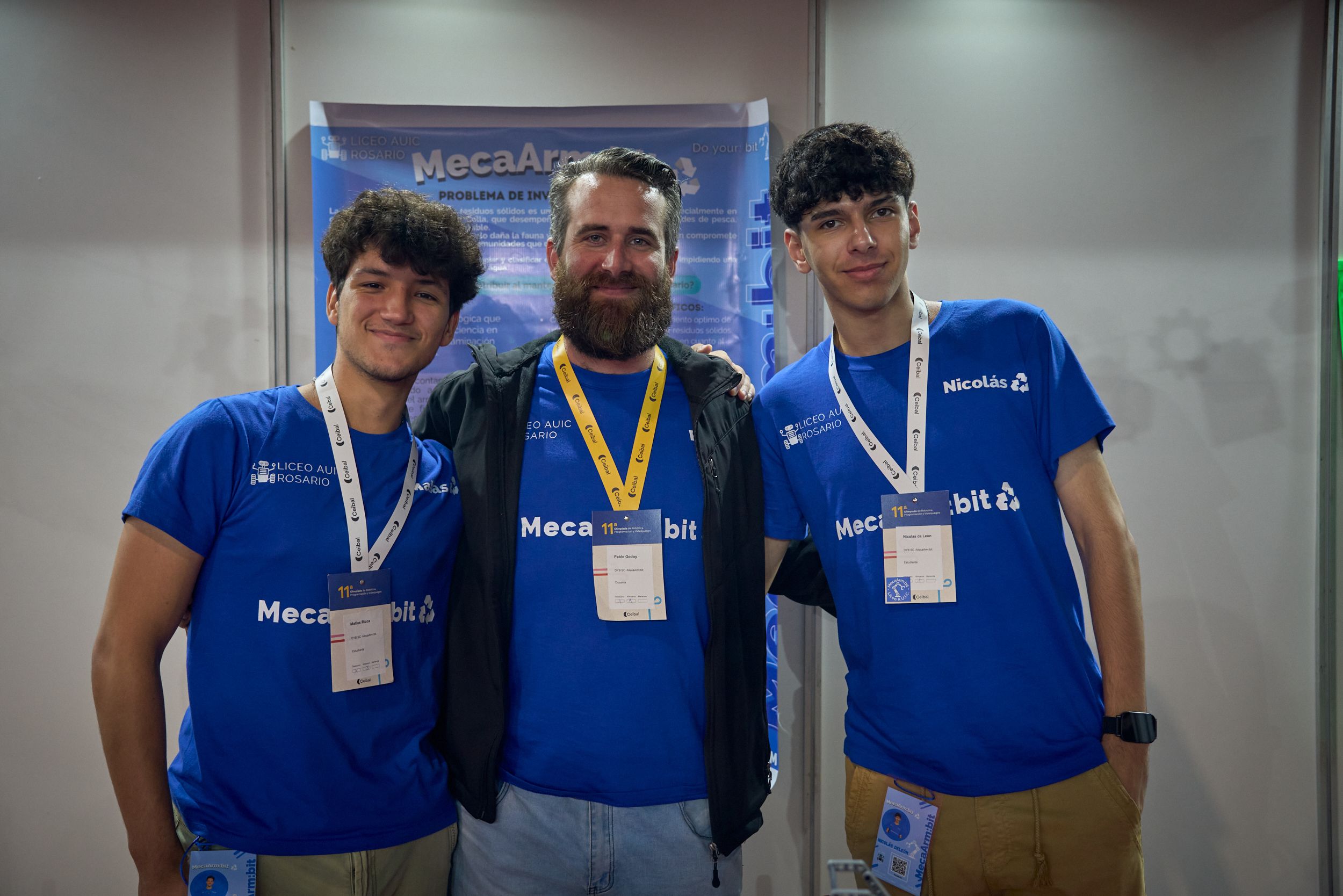 Students and teacher pose in front of a large sign for the MecaArm:bit.