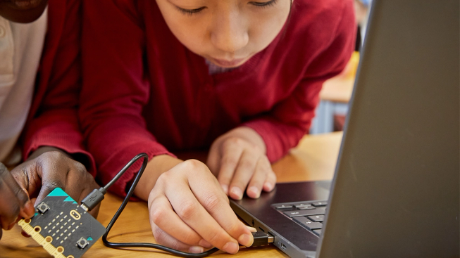 Disgybl ysgol gynradd yn plygio micro:bit i liniadur gan ddefnyddio cebl USB.