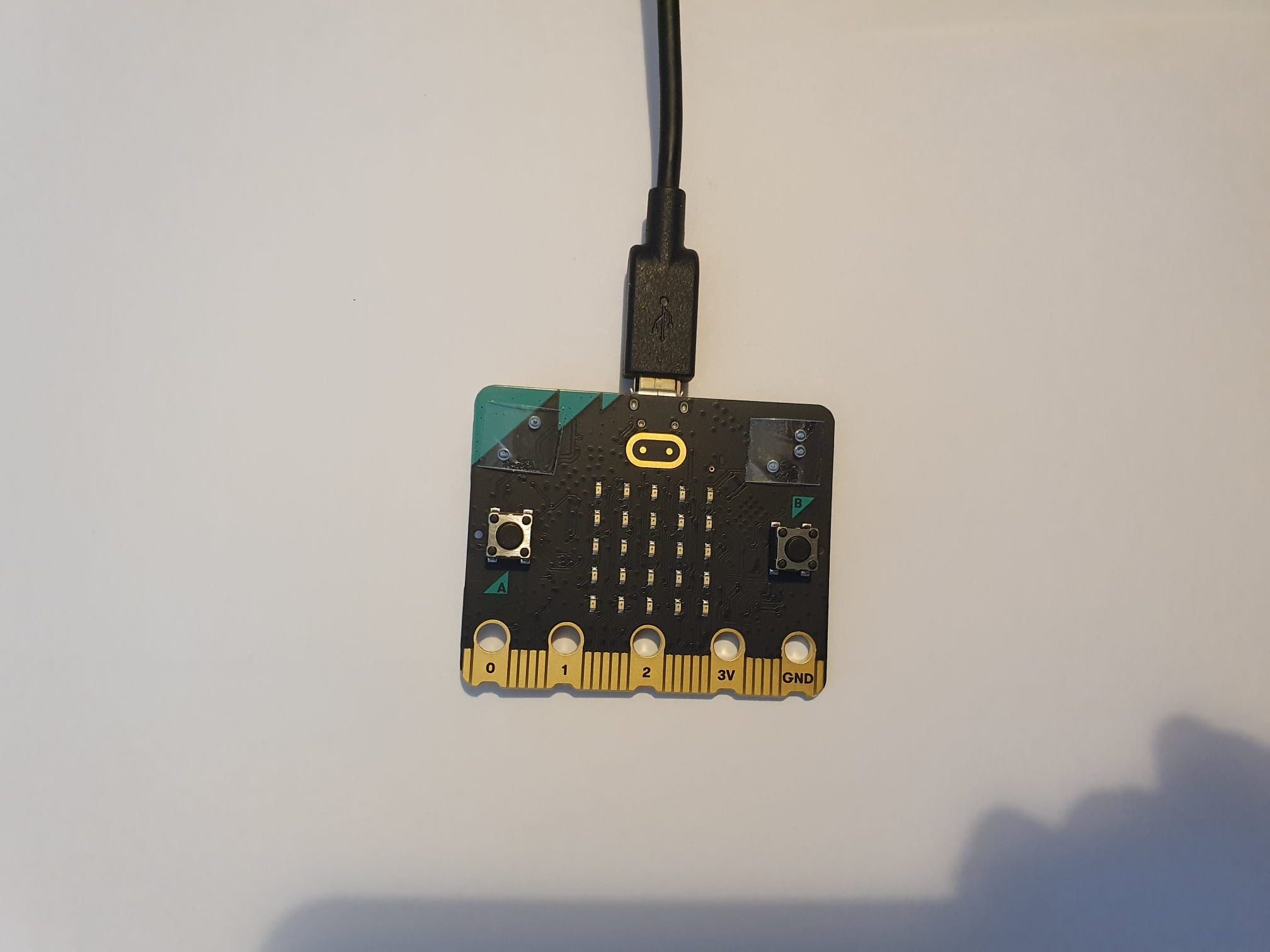 The front of a micro:bit with braille capital A and B labels above the buttons.