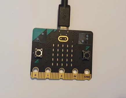 The front of a micro:bit with braille capital A and B labels above the buttons.